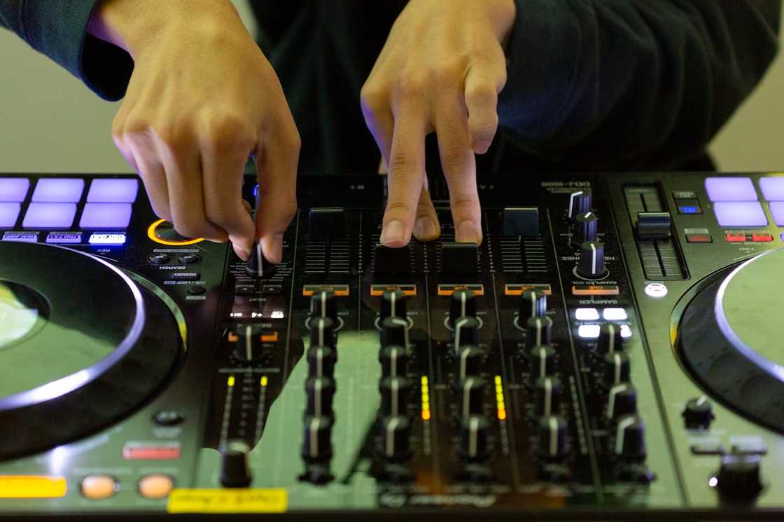A close-up of a DJ's hands adjusting knobs and sliders on a lit-up mixer during a live set.