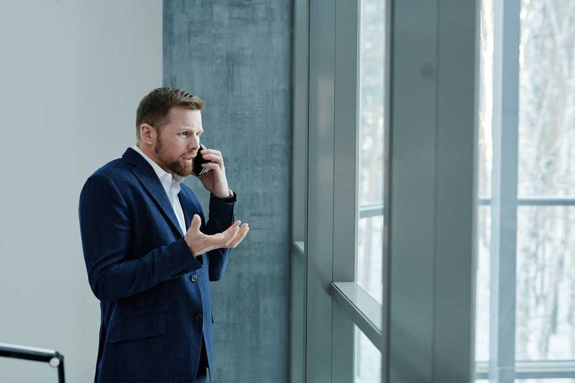 A man stands by a window talking on his phone.