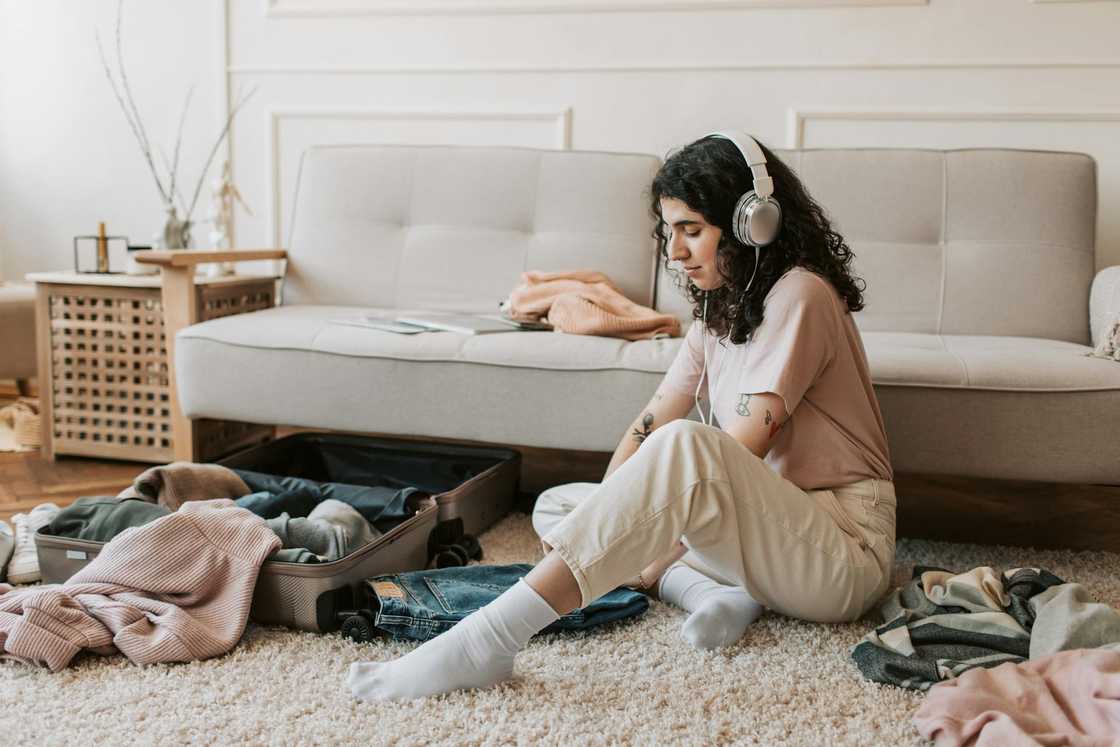 A woman listens to music through her headphones while packing clothes into a suitcase on the floor. A woman listens to music through her headphones while packing clothes into a suitcase on the floor.