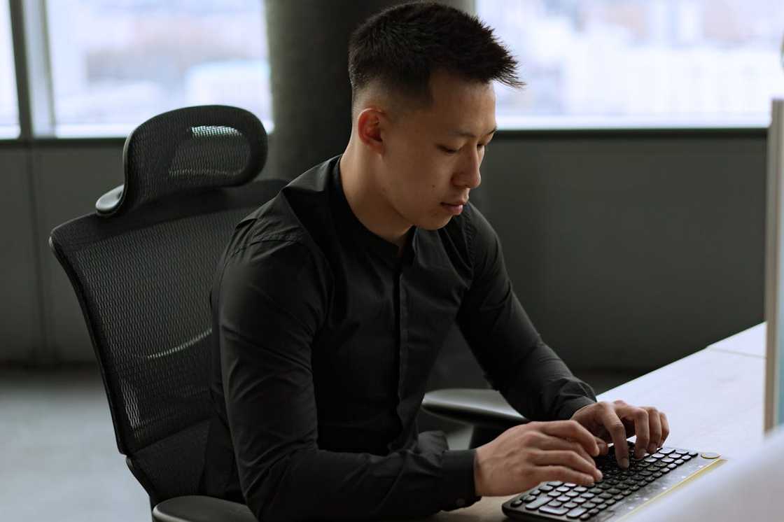 A man is working at a desk, typing on a keyboard in a modern office.