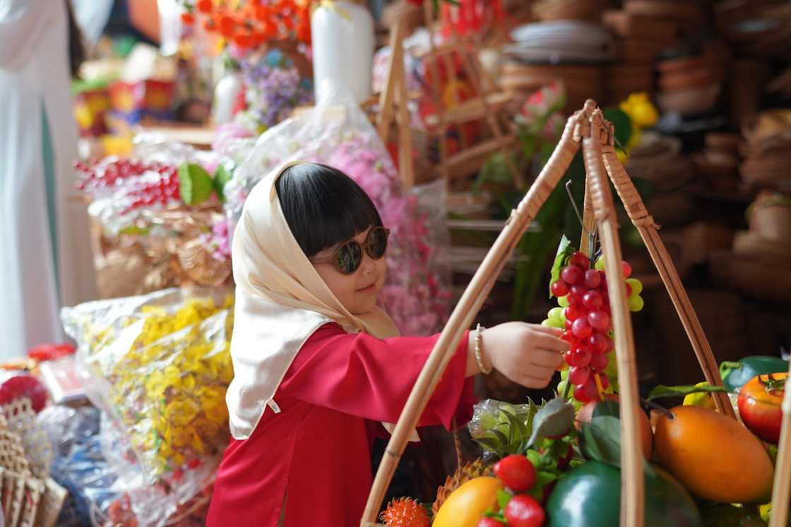 A young child reaches for grapes at a colourful market stall filled with fruits and flowers. A young child reaches for grapes at a colourful market stall filled with fruits and flowers.