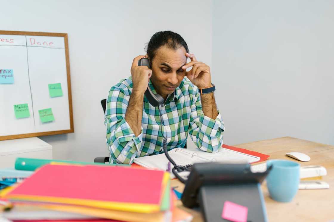A man looks stressed while talking on a phone in an office.