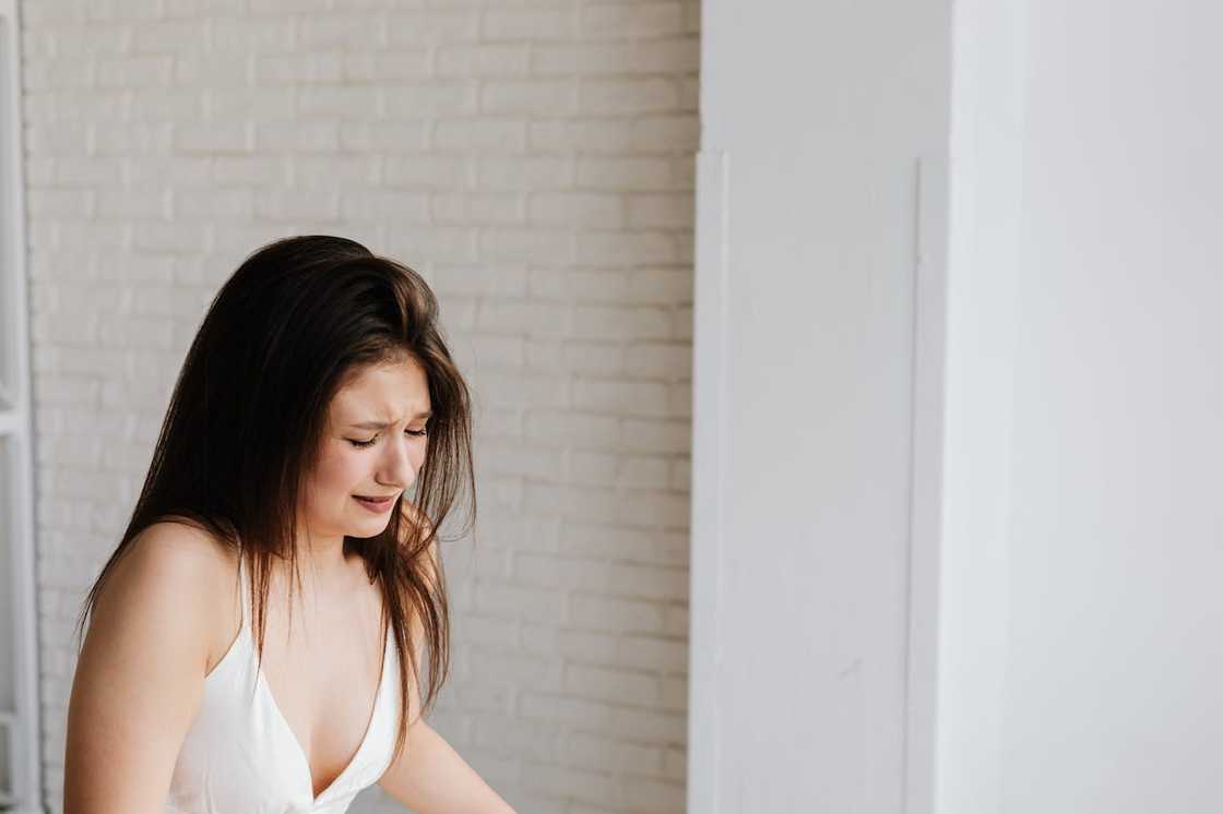 A woman cries while standing indoors against a light-coloured wall. A woman cries while standing indoors against a light-coloured wall.