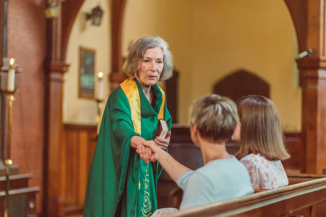 A female pastor shakes congregants hands in a church setting.