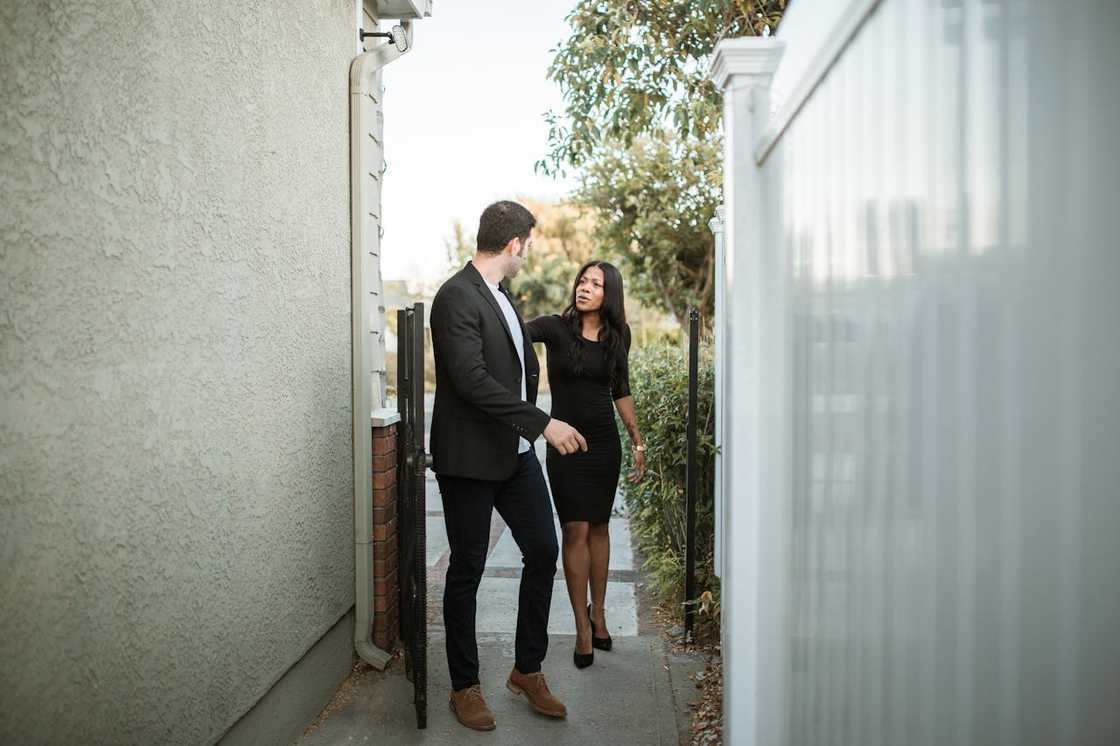 A man and a woman walk through a narrow outdoor passage while talking.