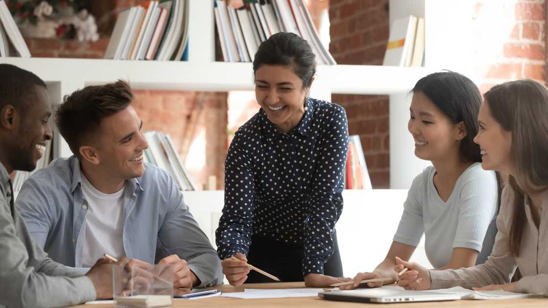 A coach smiles as trainees laugh during a voice training session.