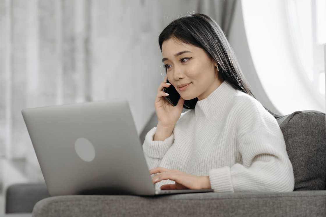 A woman talks on a phone while working on a laptop at home. A woman talks on a phone while working on a laptop at home.