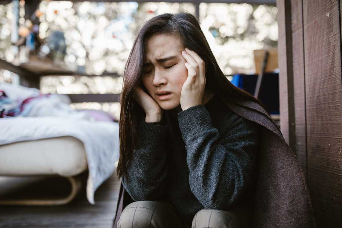 A woman sitting indoors, holding her head in distress. A woman sitting indoors, holding her head in distress.