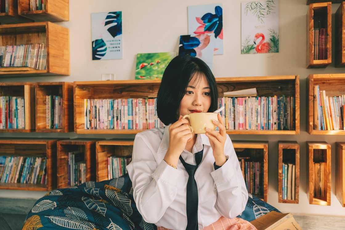A person in a white shirt and black tie holds a yellow mug while seated in a cosy reading nook.