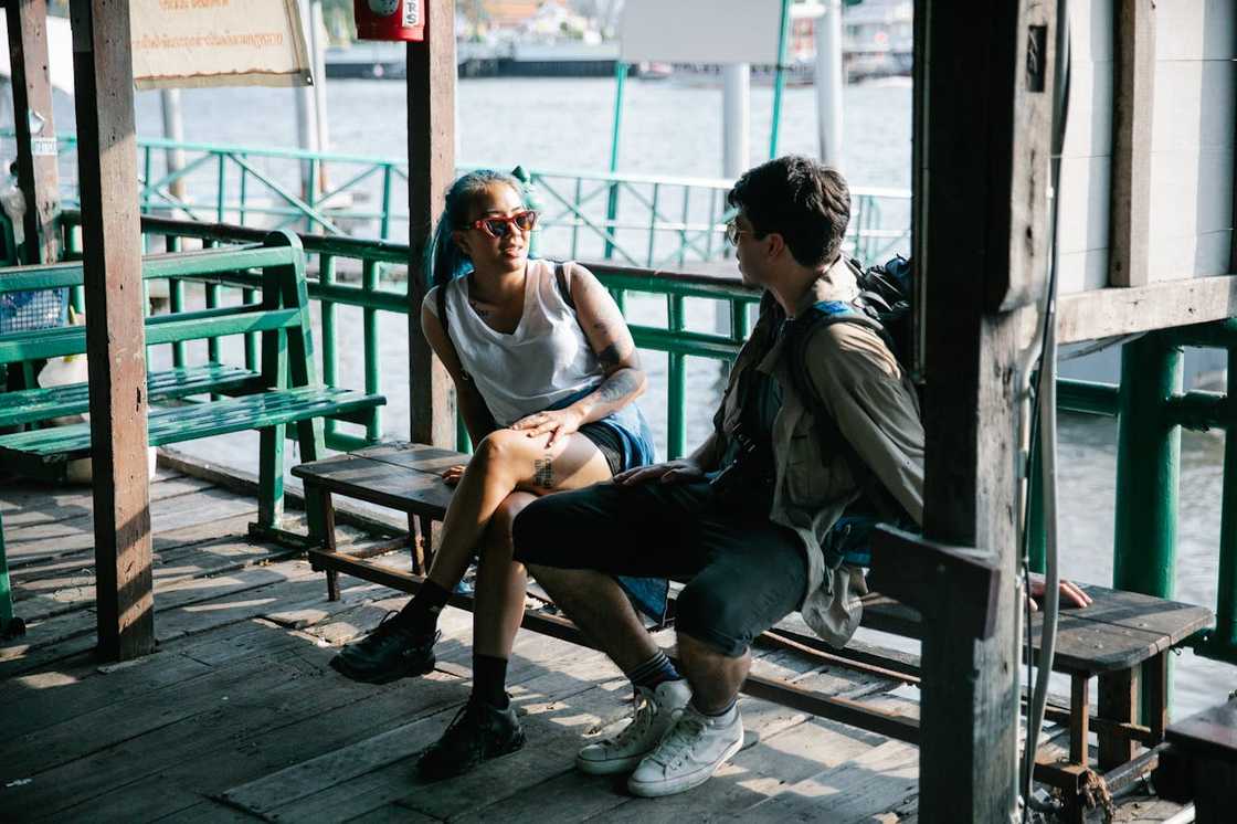 A woman and a man sit on a wooden bench at the bay.