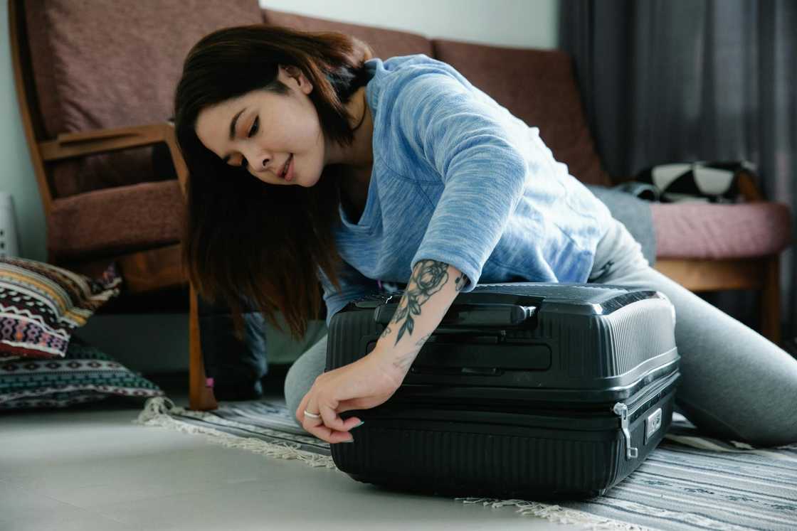 A woman zipping a suitcase at home.