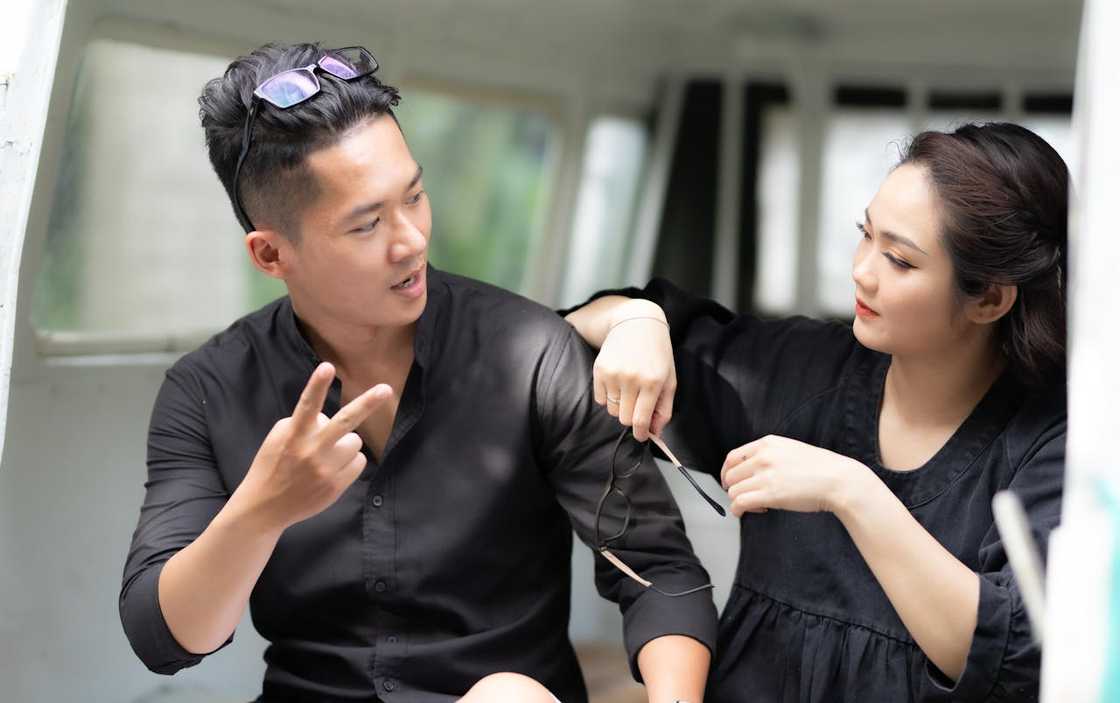 A couple talk closely indoors, one gesturing while the other holds glasses. A couple talk closely indoors, one gesturing while the other holds glasses.