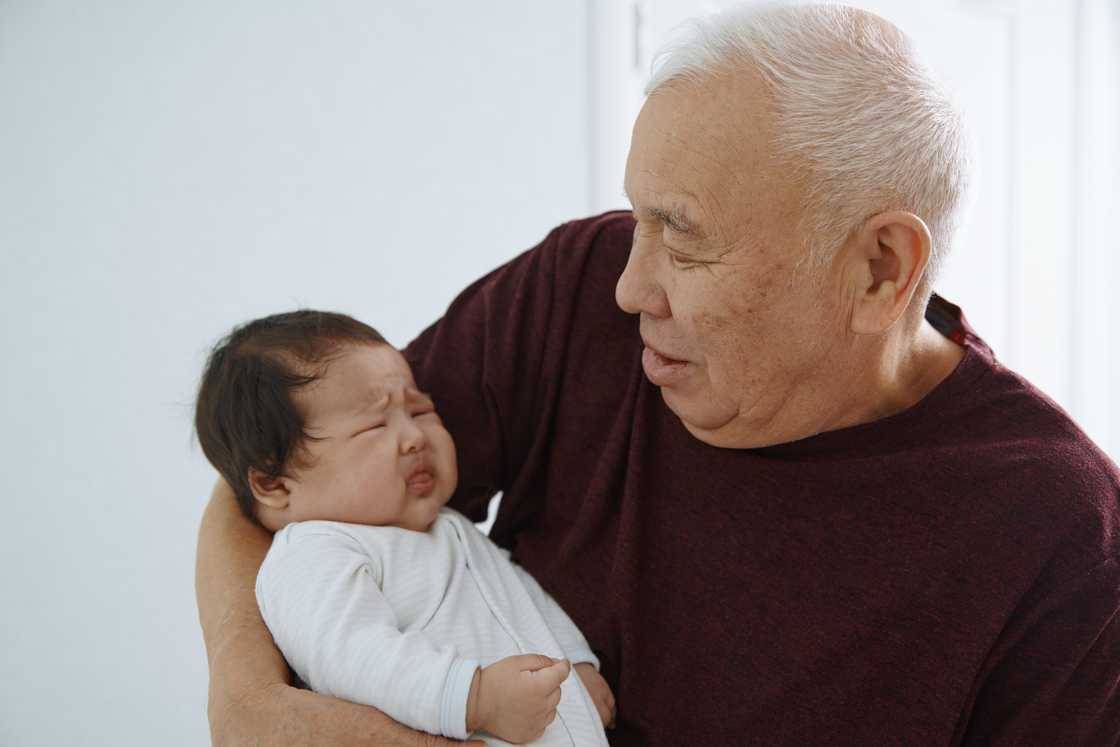 A senior man carrying his crying newborn A senior man carrying his crying newborn