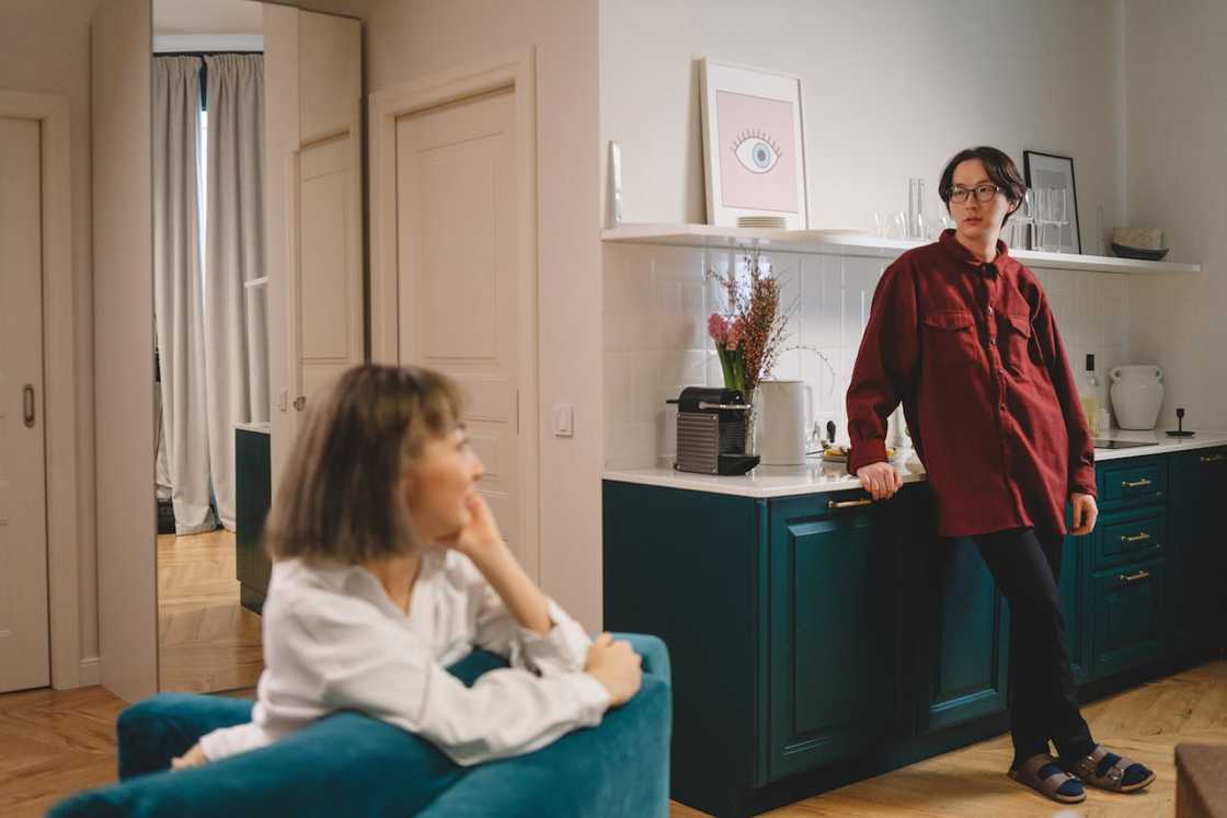 A young man and an older woman converse in the kitchen.