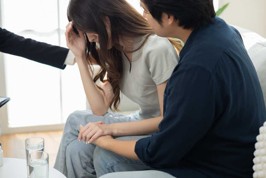 An emotional woman sitting in tears while partner comforts her