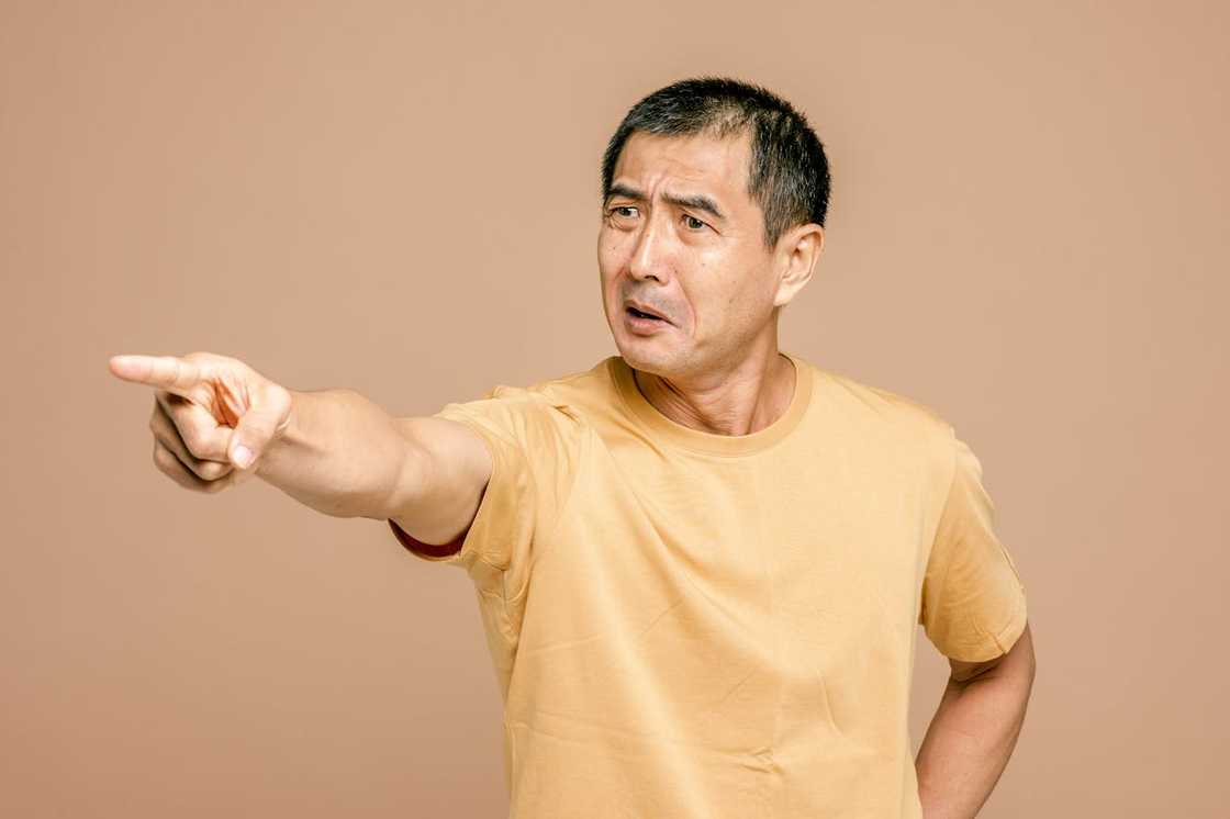 An adult in a yellow t-shirt points forward with a raised eyebrow and open mouth. An adult in a yellow t-shirt points forward with a raised eyebrow and open mouth.