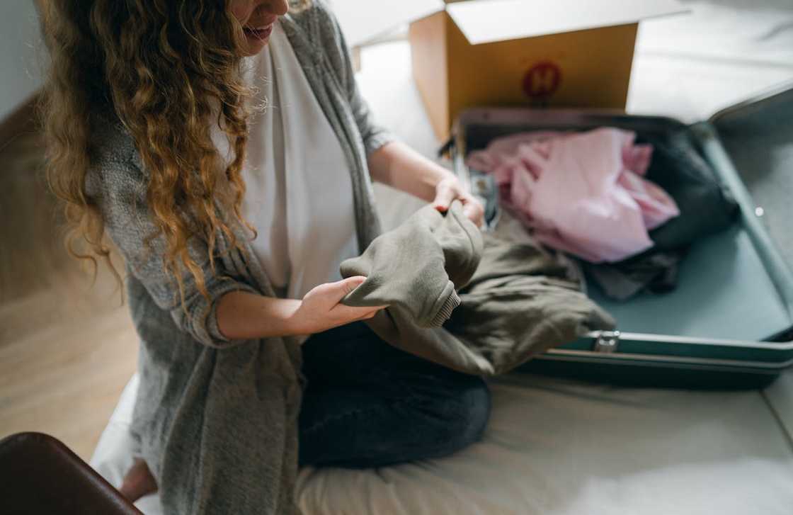 A woman kneels on the floor packing clothes into an open suitcase. A woman kneels on the floor packing clothes into an open suitcase.