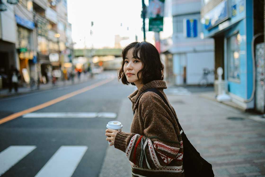 A lady crosses the road with her coffee in hand A lady crosses the road with her coffee in hand