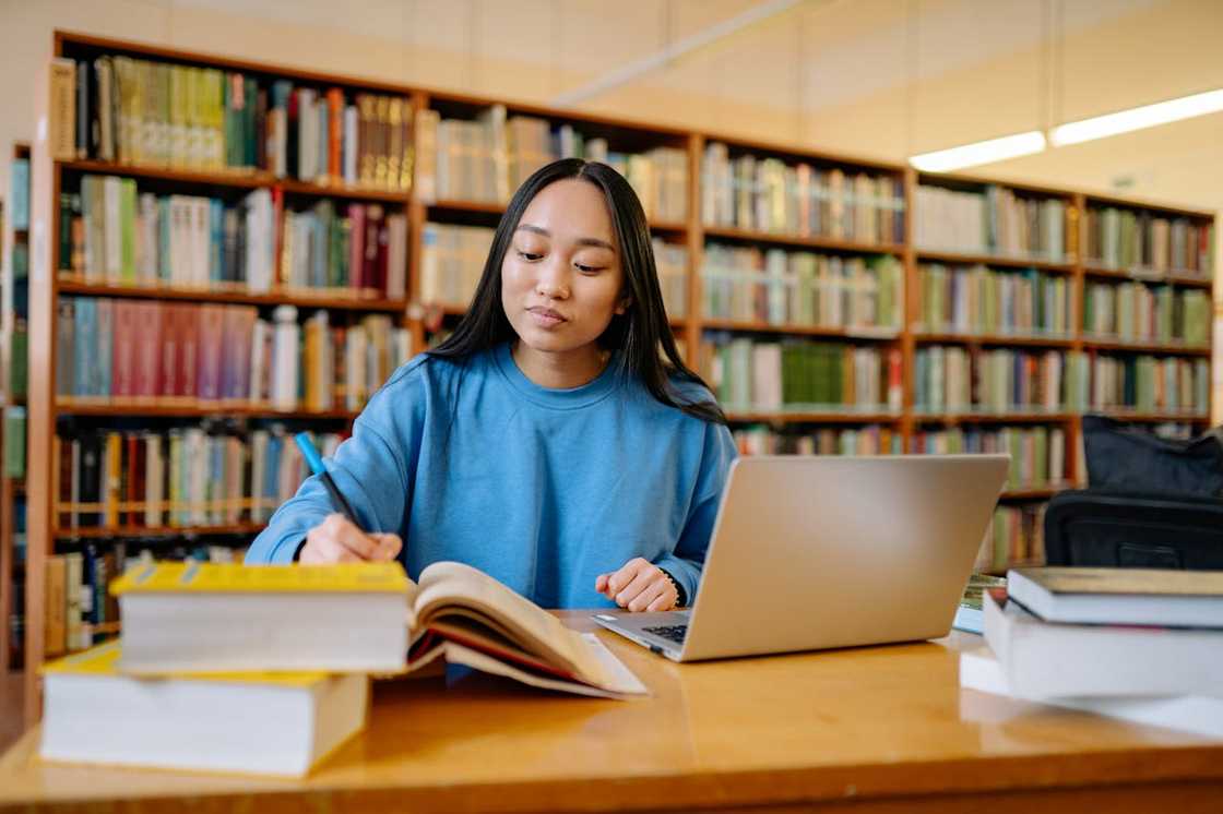 A school receptionist in a blue sweatshirt at a library table with books and a laptop. A school receptionist in a blue sweatshirt at a library table with books and a laptop.