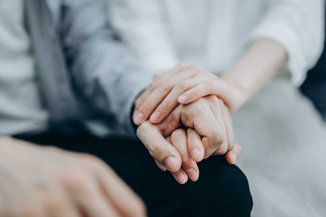 A young couple sitting on sofa compassionately holding hands
