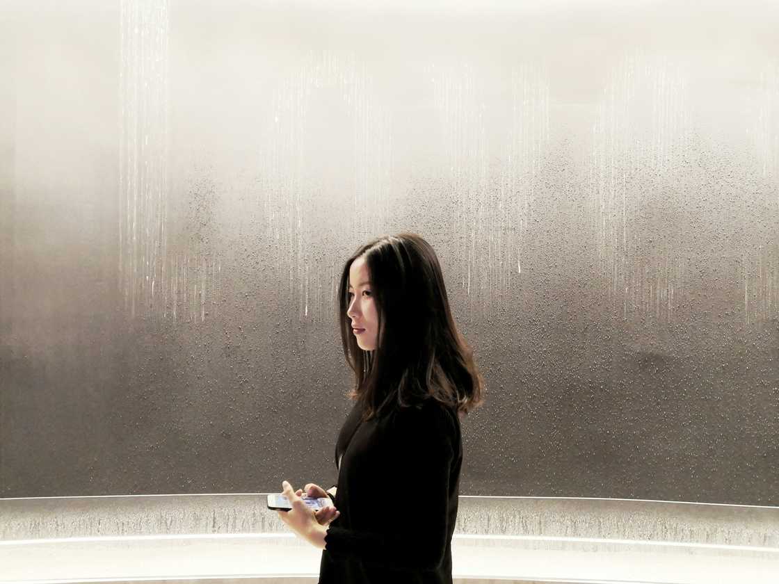 A person in dark clothes stands indoors against a misted wall with vertical water streaks.