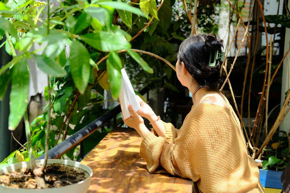 A woman reads a book while seated outdoors. A woman reads a book while seated outdoors.
