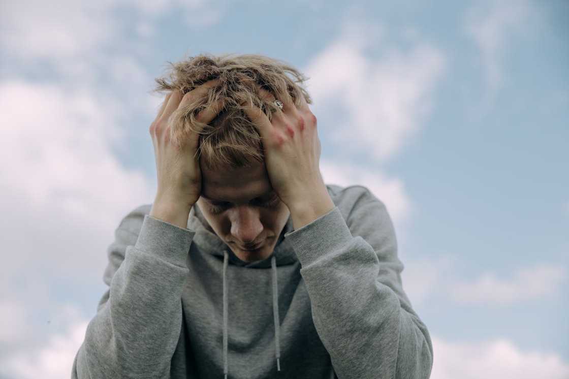 A young man in a grey hoodie holds his head in his hands. A young man in a grey hoodie holds his head in his hands.