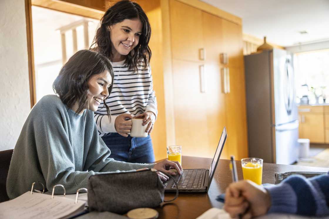 A mother and daughter are scrolling through a laptop