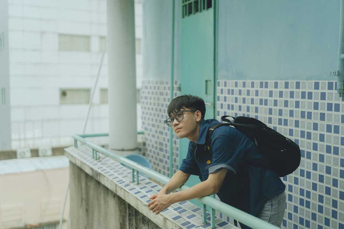 A young man with a backpack leans on a balcony railing and looks into the distance. A young man with a backpack leans on a balcony railing and looks into the distance.