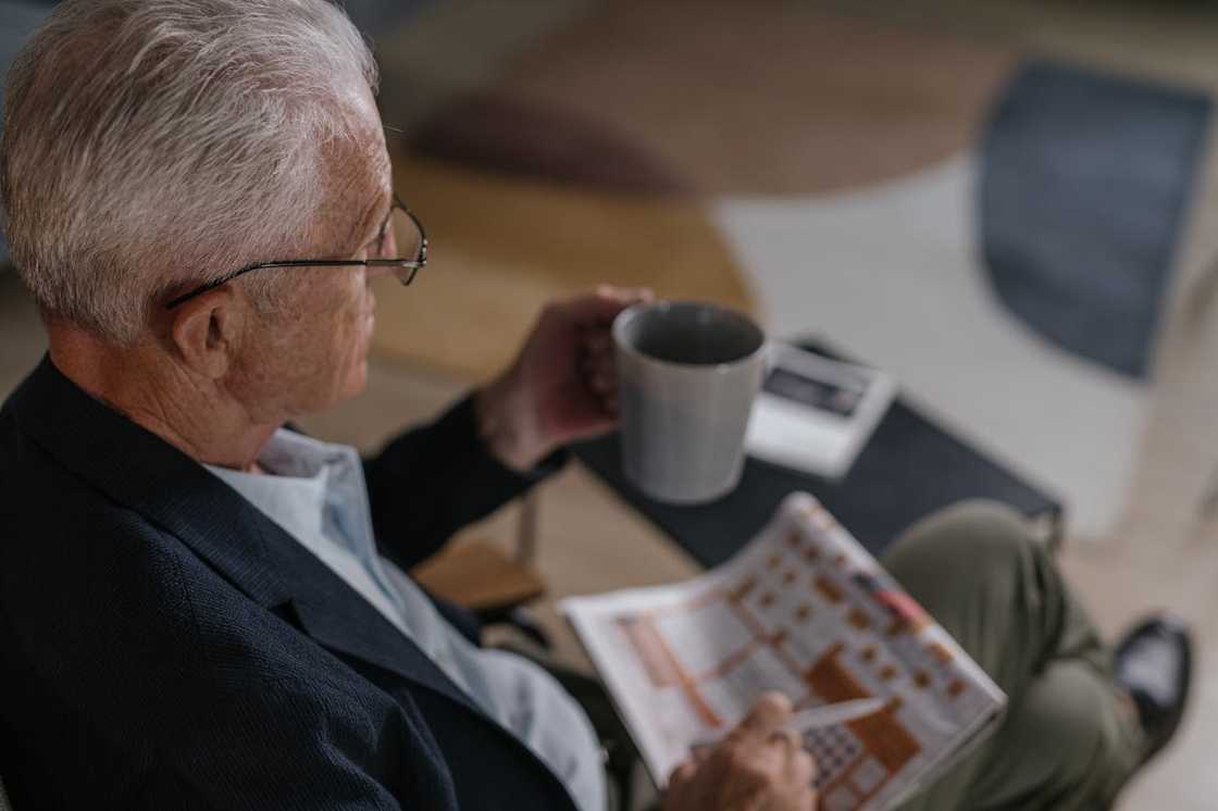 An older man holding a mug and reading a home decor magazine. An older man holding a mug and reading a home decor magazine.
