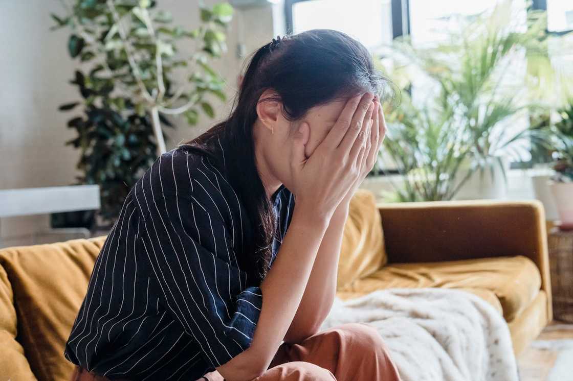 A woman in a striped shirt covers their face using their hands. A woman in a striped shirt covers their face using their hands.