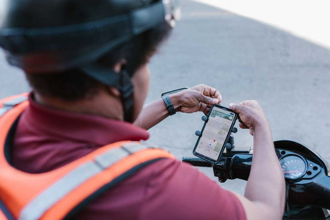 Motorbike delivery rider checking navigation on smartphone mount.