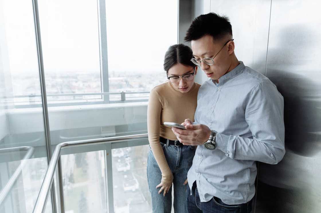 A man scrolls through a smartphone while his partner watches. A man scrolls through a smartphone while his partner watches.
