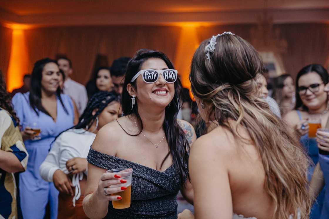 A guest wearing novelty sunglasses laughs while dancing at a lively party. A guest wearing novelty sunglasses laughs while dancing at a lively party.