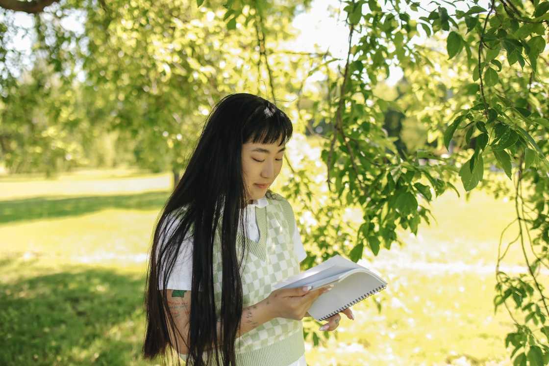 A woman sitting outdoors holding a report card and looking reflective.