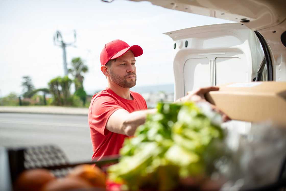 A man unloads a box of food from a van during a community food delivery.