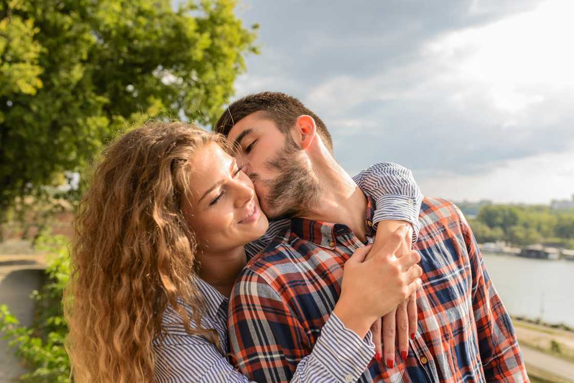 A couple embracing outdoors as a man kisses the woman's cheek. A couple embracing outdoors as a man kisses the woman's cheek.
