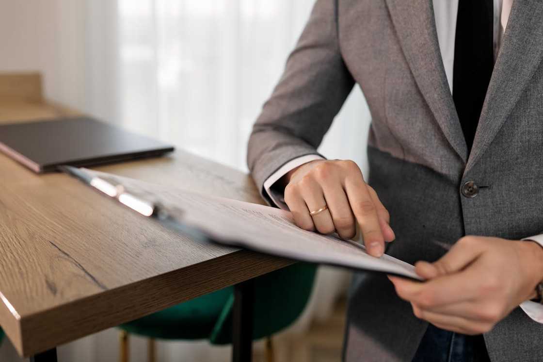 A person in a suit reviewing and pointing at a document on a clipboard. A person in a suit reviewing and pointing at a document on a clipboard.