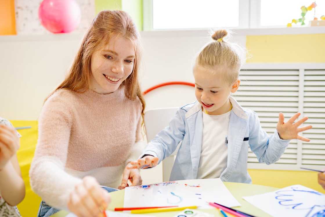 Teacher helping a young child paint during an art activity. Teacher helping a young child paint during an art activity.
