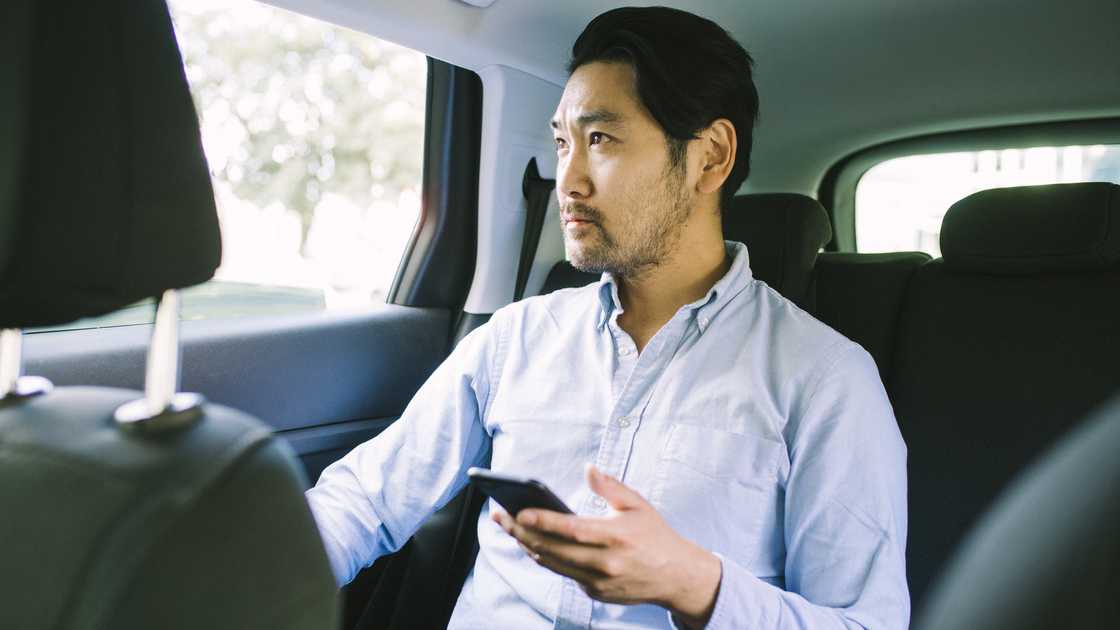 A man listening to an audio in his phone while sitting inside a car