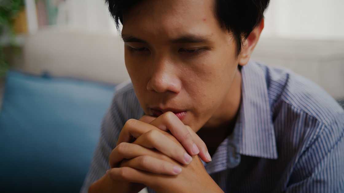 A sad young man with hands clasped.