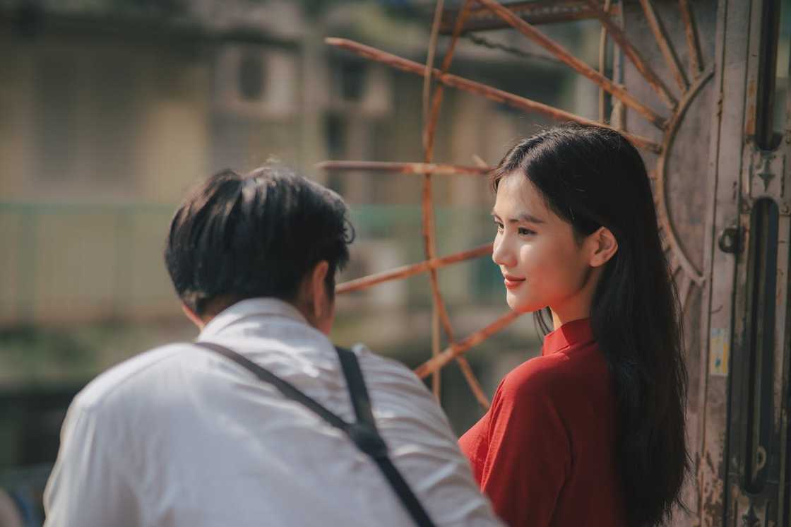 A woman in a red dress looks back calmly at a man standing beside her outdoors. A woman in a red dress looks back calmly at a man standing beside her outdoors.