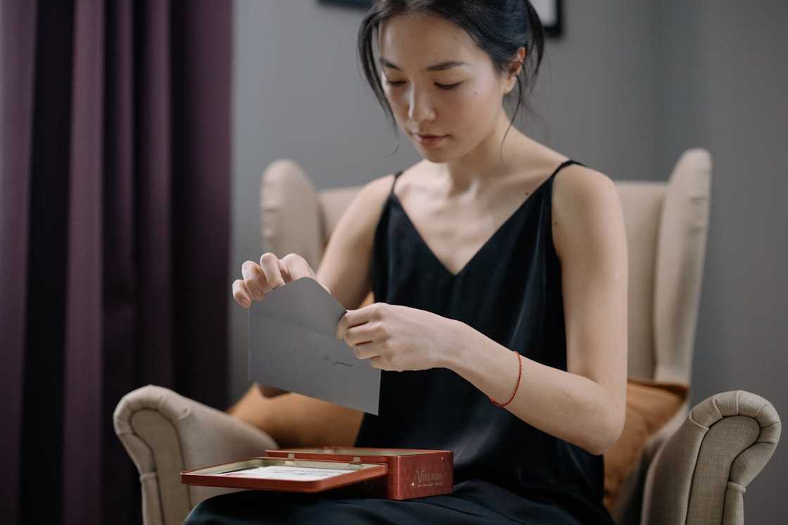 A woman quietly opens a personal letter while seated. A woman quietly opens a personal letter while seated.