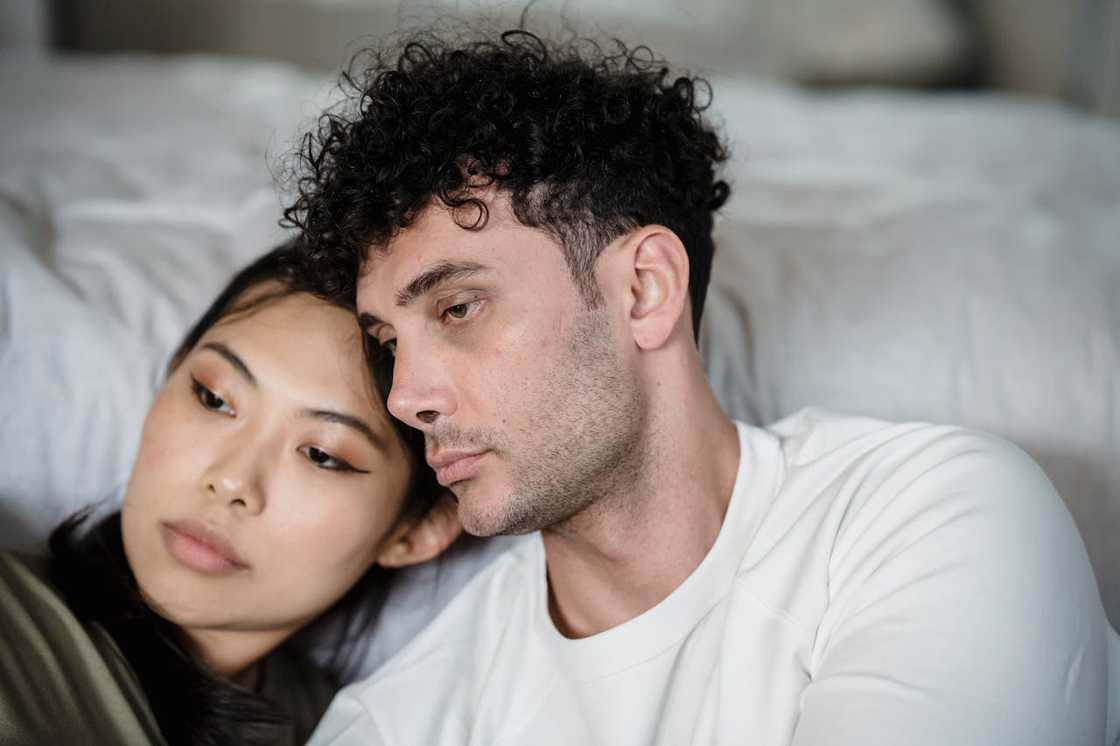 A couple sits close together, leaning on each other with calm but distant expressions.