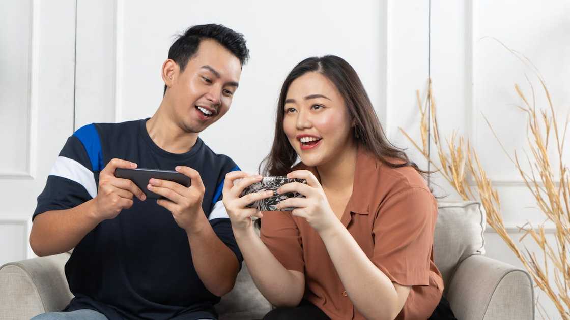Two people sit on a couch in a cosy, sunlit room, playing games on their phones. Two people sit on a couch in a cosy, sunlit room, playing games on their phones.
