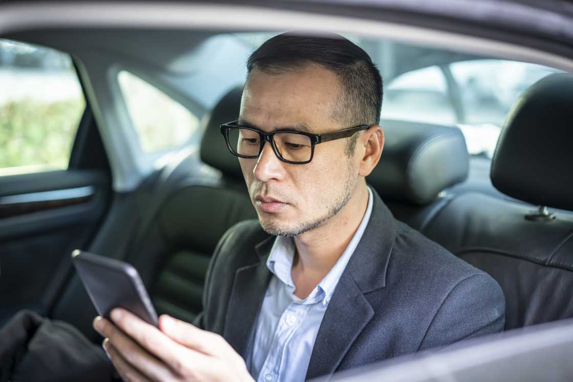 A man in glasses looking at his cell phone in the car A man in glasses looking at his cell phone in the car
