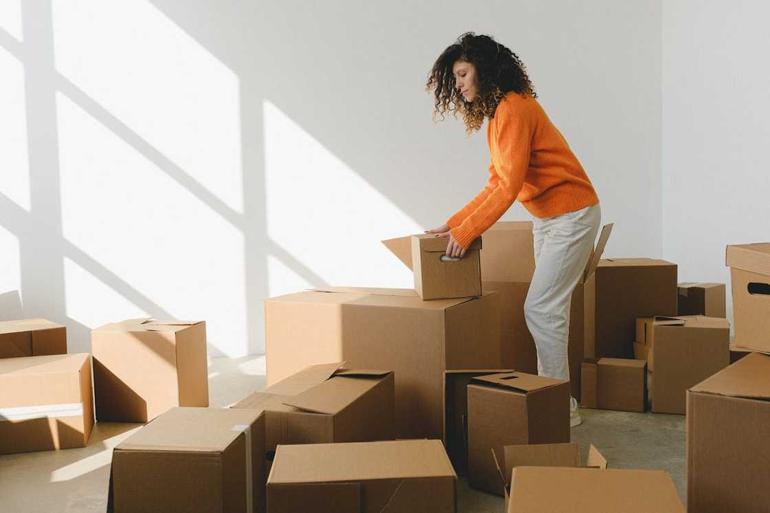 A woman stacking cardboard boxes in a bright, empty room after moving in.