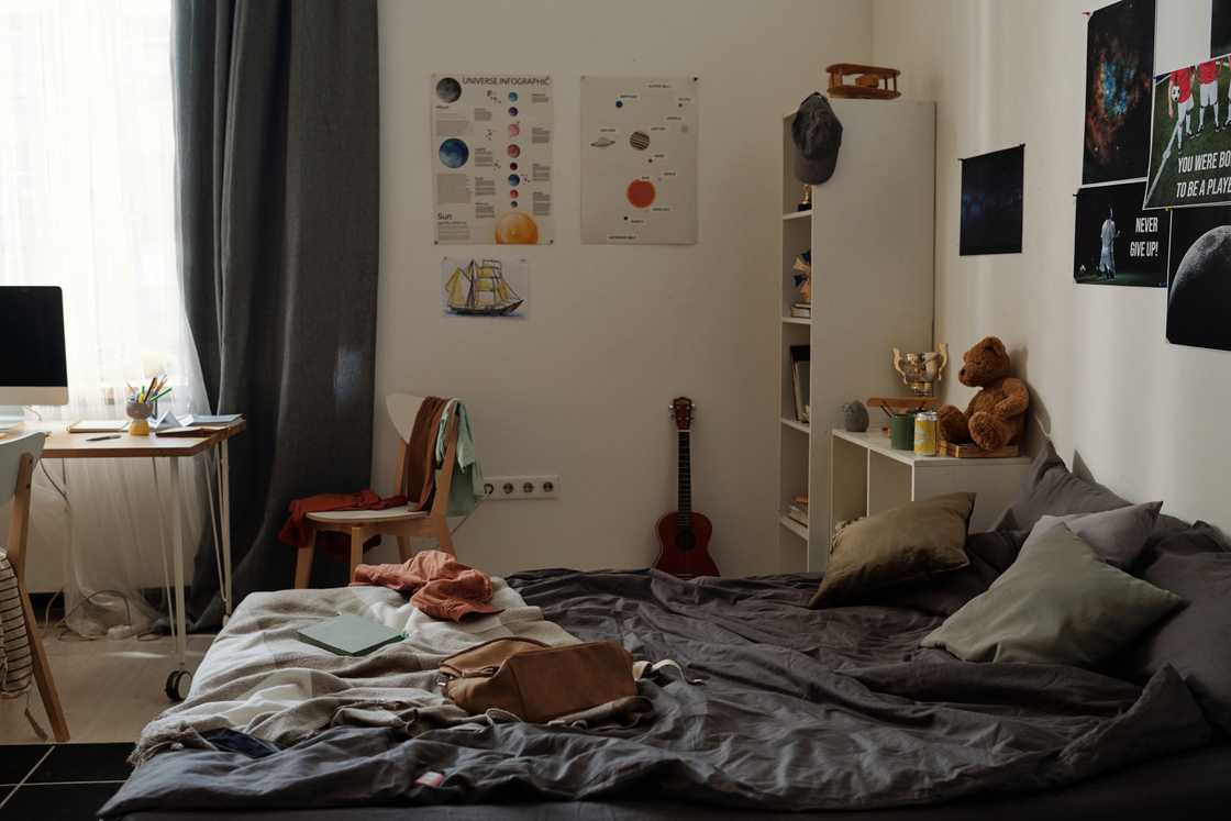 Unmade bed with study desk and science posters in a cosy bedroom.