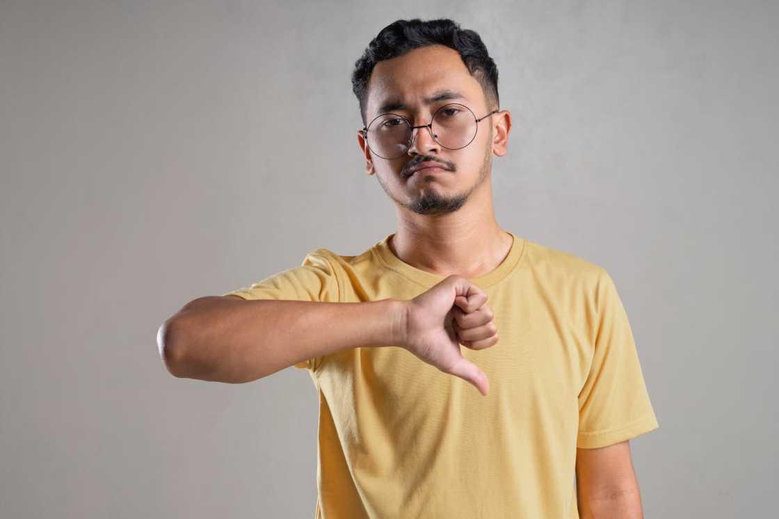 A man gives a thumbs-down gesture against a plain background. A man gives a thumbs-down gesture against a plain background.