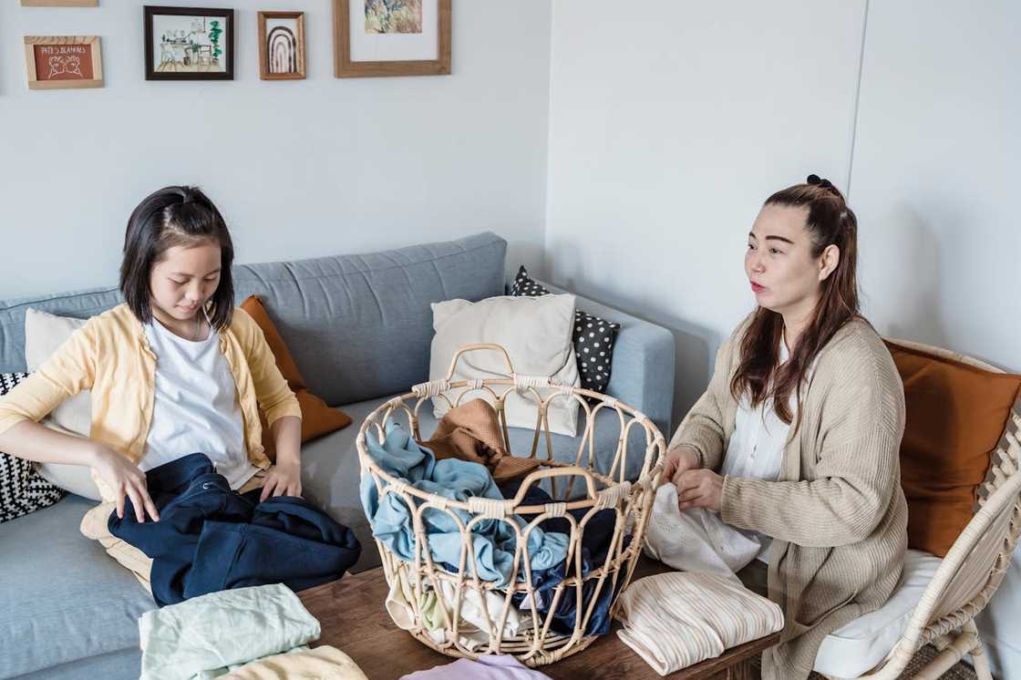 Two people fold clothes together at a table near a laundry basket. Two people fold clothes together at a table near a laundry basket.